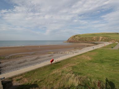 A beach with a grassy hill and a walking path along the shore at Caldhu Cottage in Holmrook