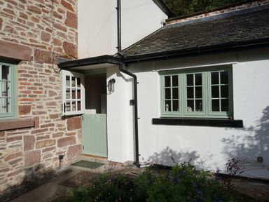 An exterior view of a building with a stone wall, green framed windows, and a green half-door at Caldhu Cottage in Holmrook