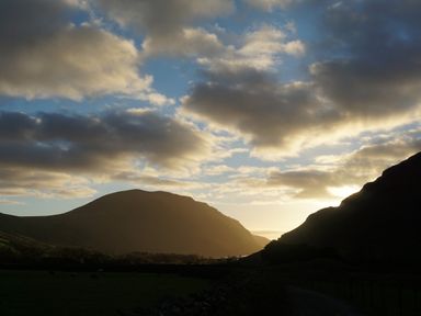 A valley with hills and a partly cloudy sky at sunset at Caldhu Cottage in Holmrook