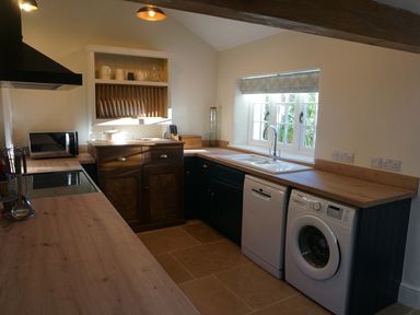 A kitchen with wooden countertops a sink dishwasher washing machine and window at Caldhu Cottage in Holmrook