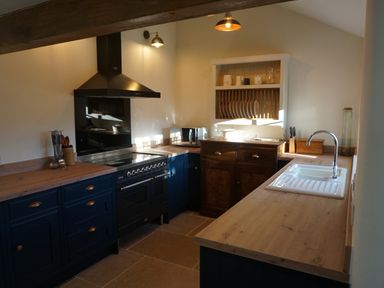 A kitchen with wooden countertops blue cabinets a black stove white sink and a dish rack at Caldhu Cottage in Holmrook