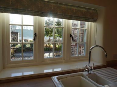 A kitchen sink with a chrome faucet under a window with a patterned valance at Caldhu Cottage in Holmrook