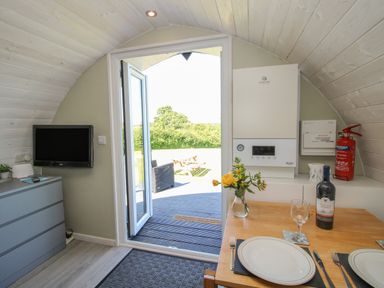 A small dining area with a table set for two a wall-mounted tv and an open door leading outside at Cherry Pod in Hookagate near Meole Brace