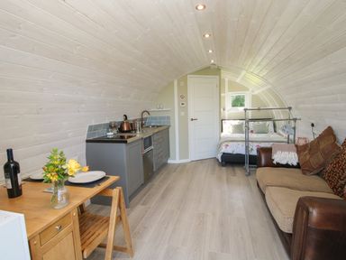 An interior view of a small pod with a kitchenette a dining table a sofa a bed and a door at Cherry Pod Hookagate near Meole Brace