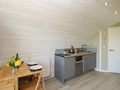 A kitchen area with grey cabinets and a wooden dining table with plates and flowers at Cherry Pod in Hookagate near Meole Brace