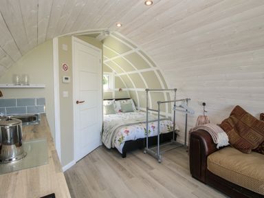 A room with a bed with floral bedding a brown sofa with cushions a clothes rack and a kitchenette at Cherry Pod in Hookagate near Meole Brace
