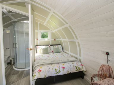 A bedroom with a bed and floral bedding and an attached bathroom with a shower at Cherry Pod in Hookagate near Meole Brace