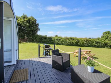 A garden with a wooden deck featuring black wicker furniture and a barbecue near a wooden picnic table at Cherry Pod in Hookagate near Meole Brace