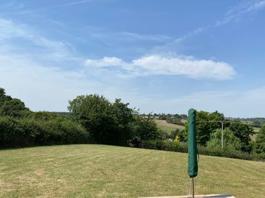 A grassy field with a covered umbrella and trees in the background at Cherry Pod in Hookagate near Meole Brace