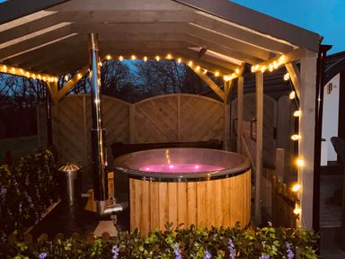 An outdoor hot tub with purple lighting under a wooden pergola with string lights at Cherry Pod in Hookagate near Meole Brace