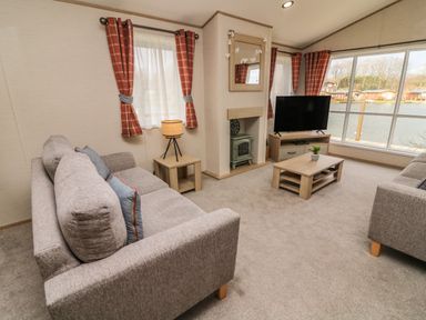 A living room with two sofas a coffee table a television and large windows overlooking water at Elim South Lakeland Leisure Village near Tewitfield