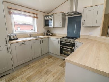 A kitchen with wooden countertops grey cabinets a stove a microwave toaster and a window at Elim South Lakeland Leisure Village near Tewitfield