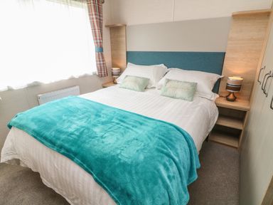 A bedroom with a double bed blue blanket and pillows two bedside tables with lamps at Elim South Lakeland Leisure Village near Tewitfield
