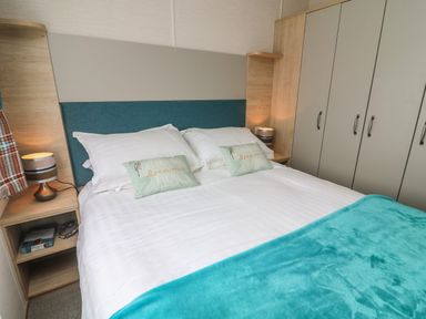 A bedroom with a double bed white pillows and teal blanket beside bedside tables and a wardrobe at Elim in South Lakeland Leisure Village near Tewitfield