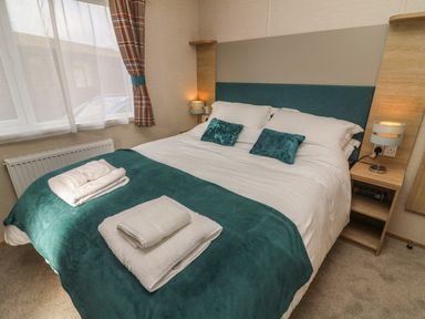A bedroom with a double bed with teal pillows and throw at Elim in South Lakeland Leisure Village near Tewitfield