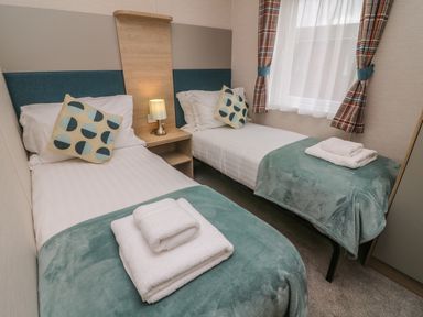 A bedroom with two single beds bedside table with a lamp and a window at Elim in South Lakeland Leisure Village near Tewitfield