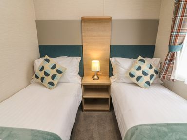 A bedroom with two single beds a bedside table and a lamp at Elim South Lakeland Leisure Village near Tewitfield