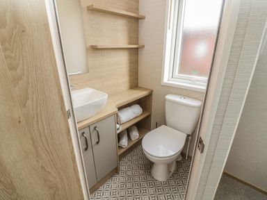 A bathroom with a toilet a sink with cabinet shelves and a window at Elim in South Lakeland Leisure Village near Tewitfield