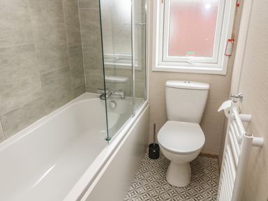 A bathroom with a bathtub toilet window and towel radiator at Elim South Lakeland Leisure Village near Tewitfield