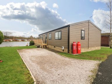 A gravel driveway beside a brown mobile home with red gas cylinders near a lake at Elim in South Lakeland Leisure Village near Tewitfield