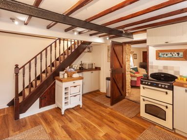 A kitchen with wooden stairs a white oven and an open wooden door leading to a living room at Southcott Farm Cottage in Sheldon