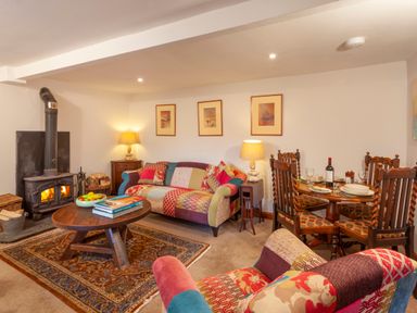 A living room with a wood-burning stove a round wooden coffee table and patterned sofas at Southcott Farm Cottage in Sheldon