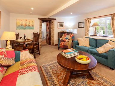 A living room with patchwork sofas a wooden coffee table and dining table set at Southcott Farm Cottage in Sheldon