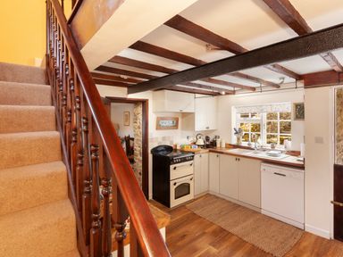 A kitchen with wooden beams a staircase and white cabinets at Southcott Farm Cottage in Sheldon
