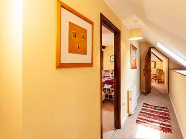 A hallway with yellow walls a striped rug a framed picture a radiator and views into a bedroom and a sitting area at Southcott Farm Cottage in Sheldon