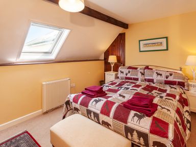 A bedroom with a double bed with patterned bedding and red towels on it two bedside tables with lamps a skylight window and a wooden door at Southcott Farm Cottage in Sheldon