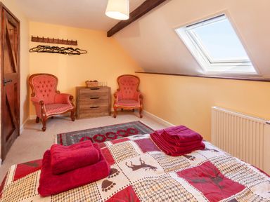 A bedroom with two red patterned armchairs a wooden chest of drawers a skylight window and red towels on a bed at Southcott Farm Cottage in Sheldon