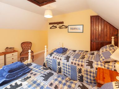 A bedroom with two beds wooden door and chair at Southcott Farm Cottage in Sheldon