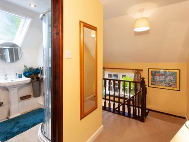 A hallway with a wooden staircase and a framed painting next to a bathroom with a shower and a sink at Southcott Farm Cottage in Sheldon