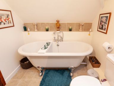 A bathroom with a clawfoot bathtub candles and framed pictures at Southcott Farm Cottage in Sheldon