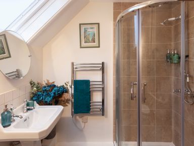 A bathroom with a sink a round mirror a shower cubicle and a towel rack with a blue towel at Southcott Farm Cottage in Sheldon