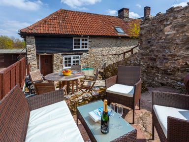 An outdoor patio with wicker furniture and a round wooden table with chairs at Southcott Farm Cottage in Sheldon