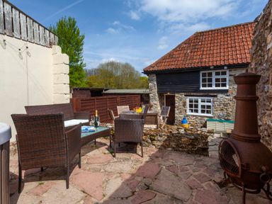 An outdoor patio with wicker chairs and tables next to a stone house with a red tiled roof at Southcott Farm Cottage in Sheldon