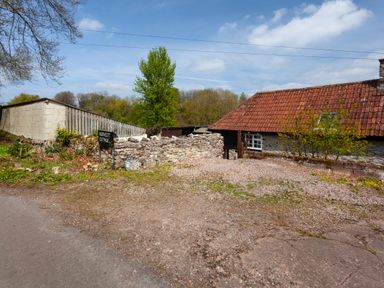 A gravel driveway with a stone wall and a sign reading Southcott Cottage next to a building with a tiled roof at Southcott Farm Cottage in Sheldon