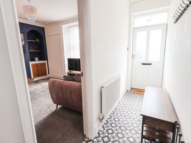 An entryway with patterned tile flooring a wooden bench and coat hooks leading to a living room with a television a sofa and built-in shelves at Aryelle House in Kendal