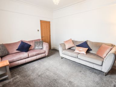 A living room with two sofas, cushions, a small table, wooden door and carpeted floor at Aryelle House in Kendal