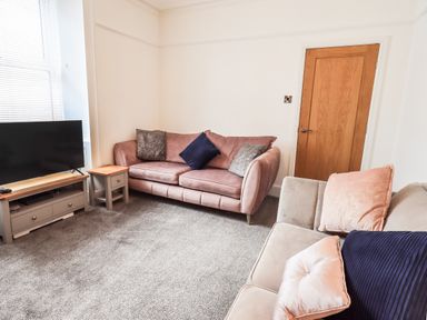 A living room with two sofas a wooden door and a television on a stand at Aryelle House in Kendal