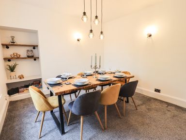 A dining room with a wooden table set for eight with mixed color chairs and decorative shelves at Aryelle House in Kendal