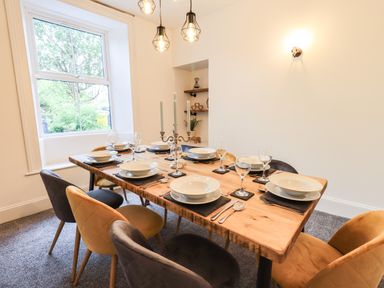 A dining room with a wooden table set with plates glasses and cutlery and multicolored chairs at Aryelle House in Kendal