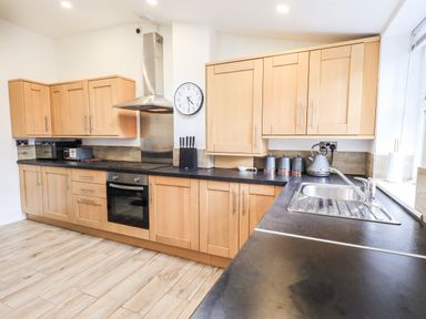A kitchen with wooden cabinets black countertops oven stove and a sink at Aryelle House in Kendal