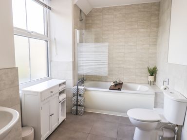 A bathroom with a bathtub a toilet a white cabinet and a window at Aryelle House in Kendal