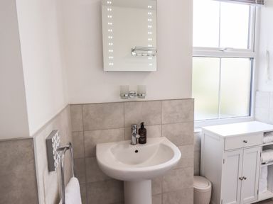 A bathroom with a pedestal sink and a mirror with lights above a white cabinet and window at Aryelle House in Kendal