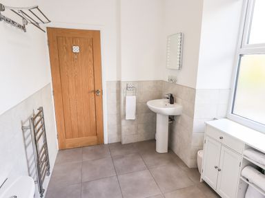 A bathroom with a wooden door pedestal sink towel rack and storage cabinet at Aryelle House in Kendal