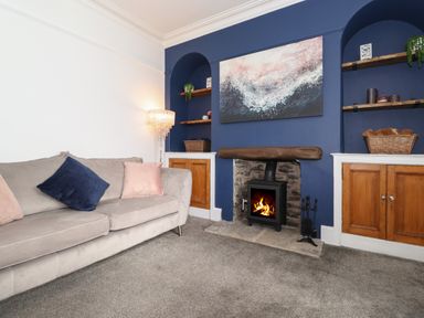 A living room with a gray sofa with pillows a fireplace with a fire and shelves with baskets at Aryelle House in Kendal