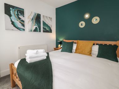 A bedroom with a wooden bed frame green and yellow cushions folded towels on bed and wall art at Aryelle House in Kendal