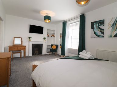 A bedroom with a bed and folded towels a dressing table a chair and a wall mounted television at Aryelle House Kendal